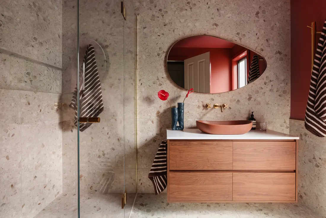 Wide view of terracotta and terrazzo bathroom with organic mirror by MNA Builds